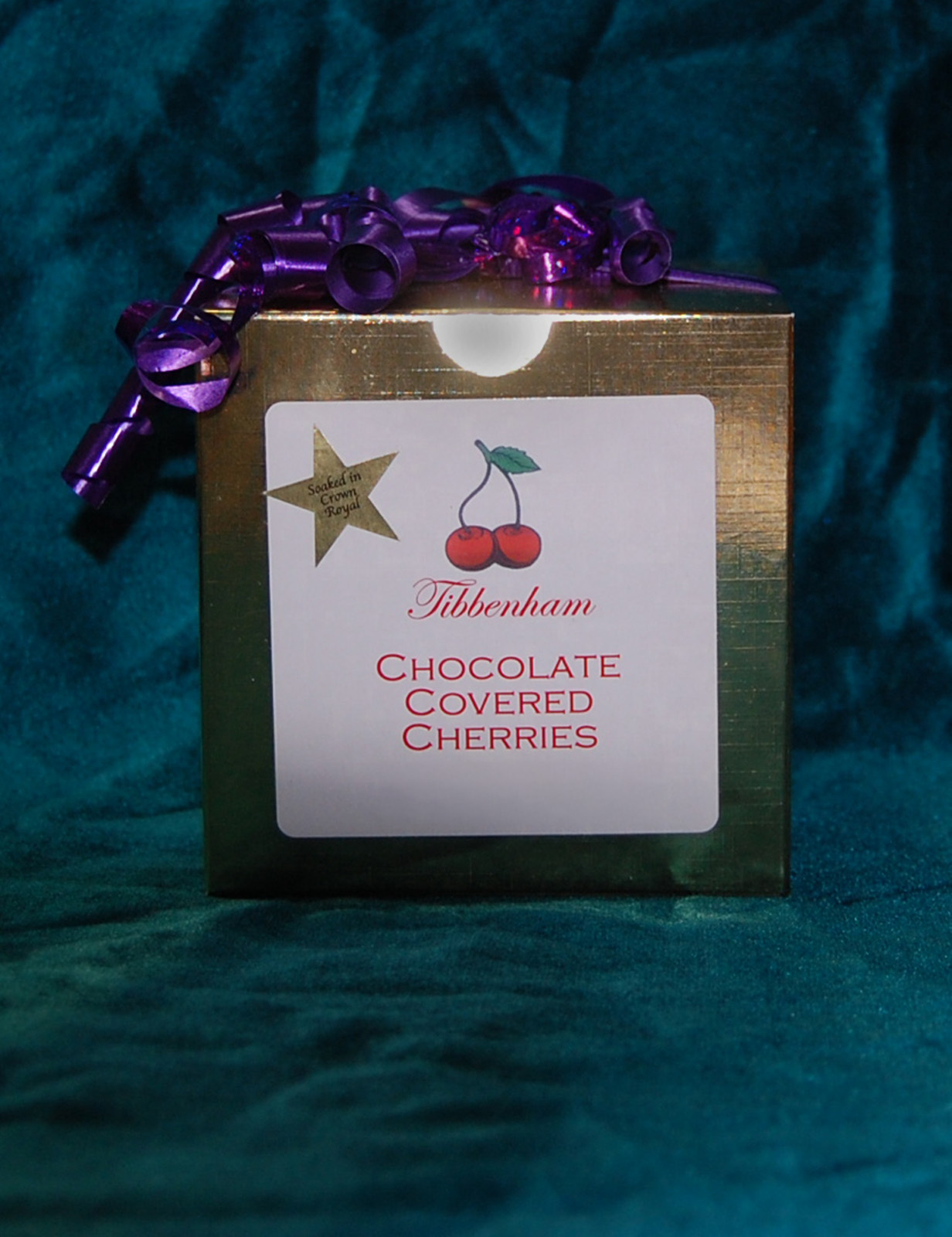 a gold box of chocolate covered cherries with a purple bow